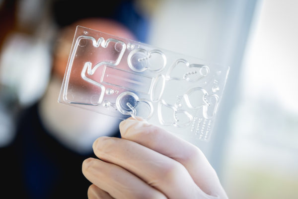 A close-up of a plastic microfluidic device held by a gowned NRC researcher at a the CRAFT research facility at the NRC campus in Boucherville, Quebec.